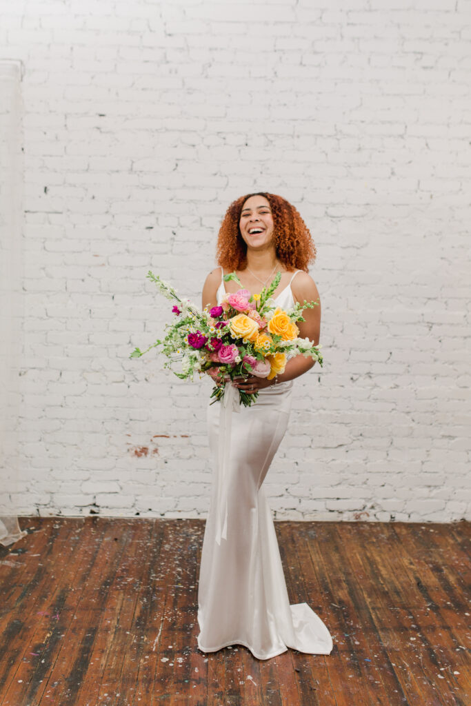 Smiling summer 2023 bride holding a bouquet in a bright floral color palette of pink, yellow and white